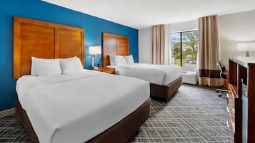 A hotel room with two beds, a desk, a lamp, and a view of the outdoors.