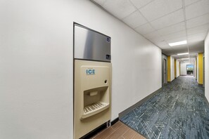 A hallway with a wall-mounted ice dispenser, a tiled floor, and a door at the end. - Comfort Inn Plainfield - Indianapolis Airport (Plainfield)