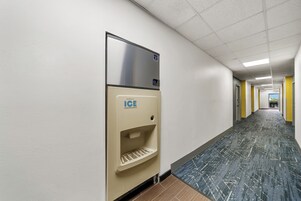 A hallway with a wall-mounted ice dispenser, a tiled floor, and a door at the end.