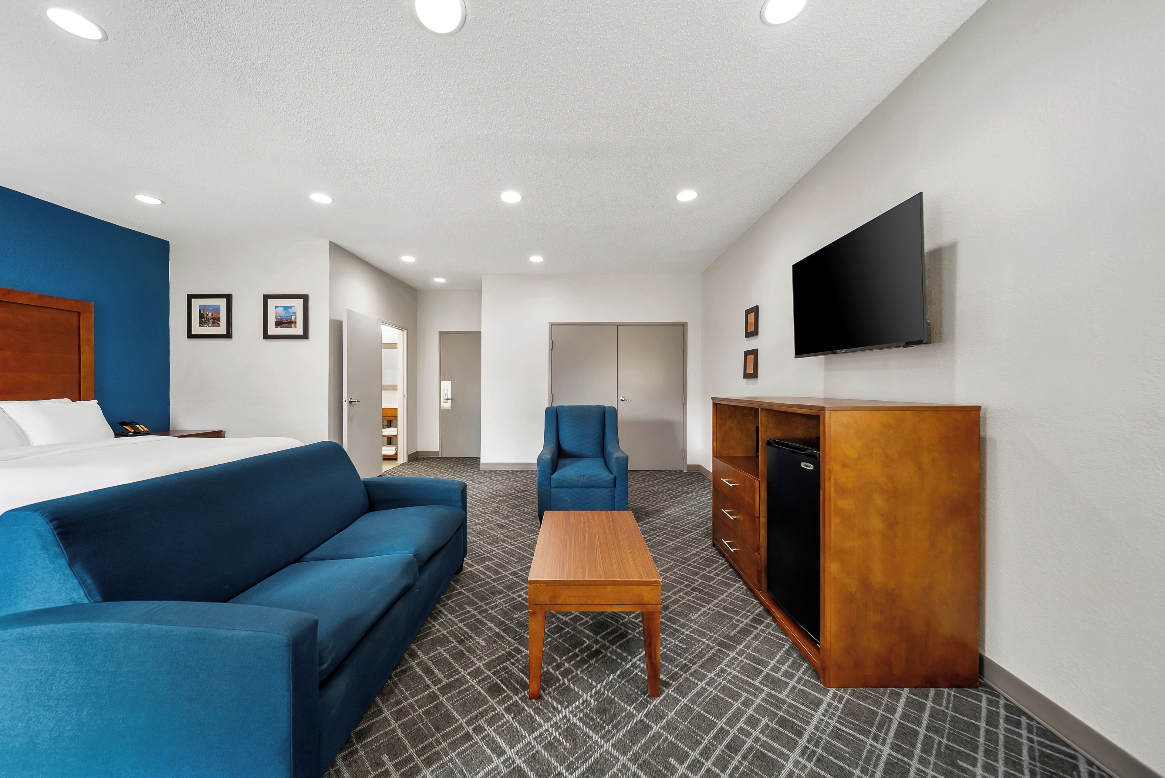 A hotel room with a bed, a blue sofa, a wooden table, a TV, and a wardrobe.