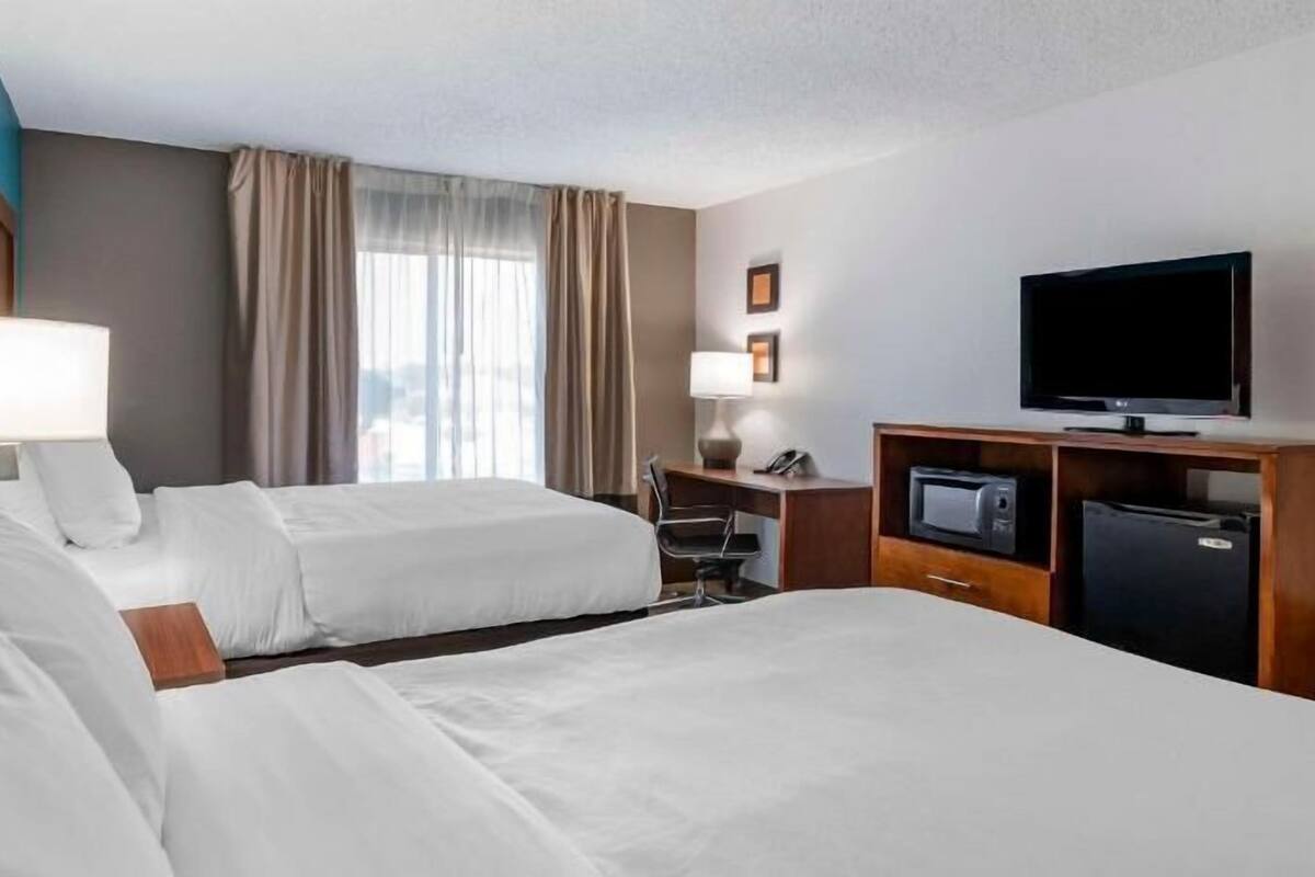 Quarto de hotel com duas camas, uma escrivaninha com computador, televisão e minibar.