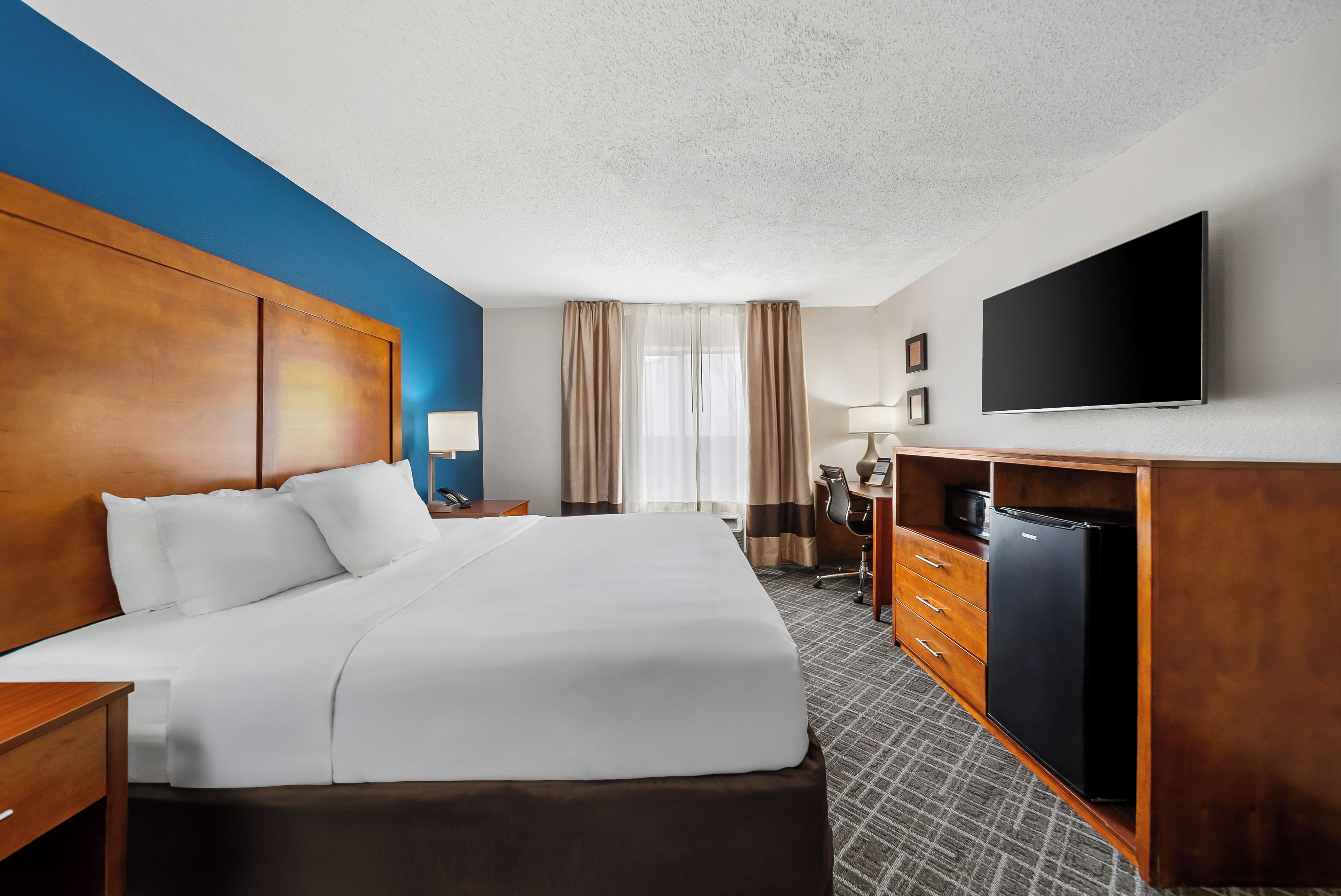 A hotel room with a large bed, a desk with a chair, a flat-screen TV, and a minibar.