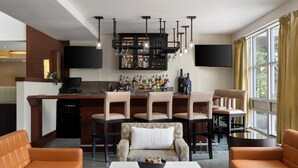 A modern kitchen with a bar area, bar stools, and a seating area with a sofa and chairs. - DoubleTree by Hilton Hotel Boston Bayside (Boston)
