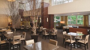 A spacious indoor dining area with multiple tables and chairs, a large potted plant, and large windows allowing natural light. - DoubleTree by Hilton Hotel Boston Bayside (Boston)