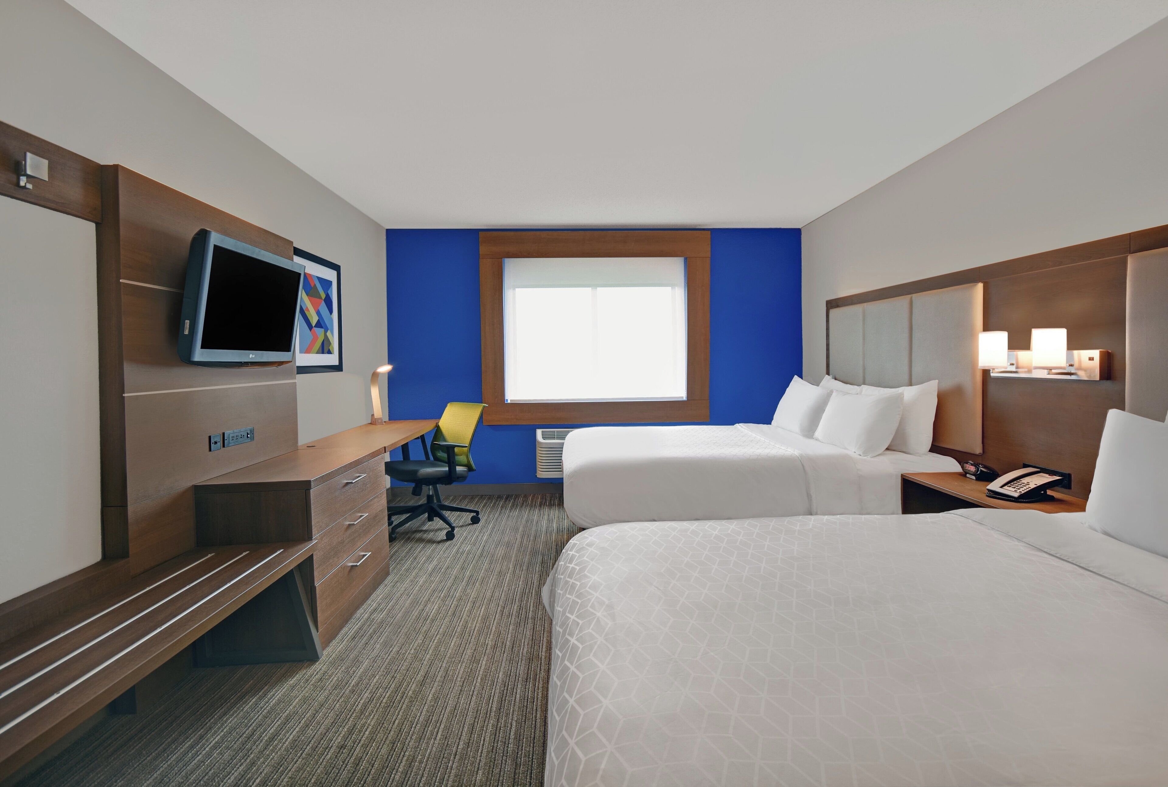 Ein Hotelzimmer mit zwei Betten, einem Schreibtisch, einem Stuhl, einem Fernseher, einem Fenster und einem Telefon.