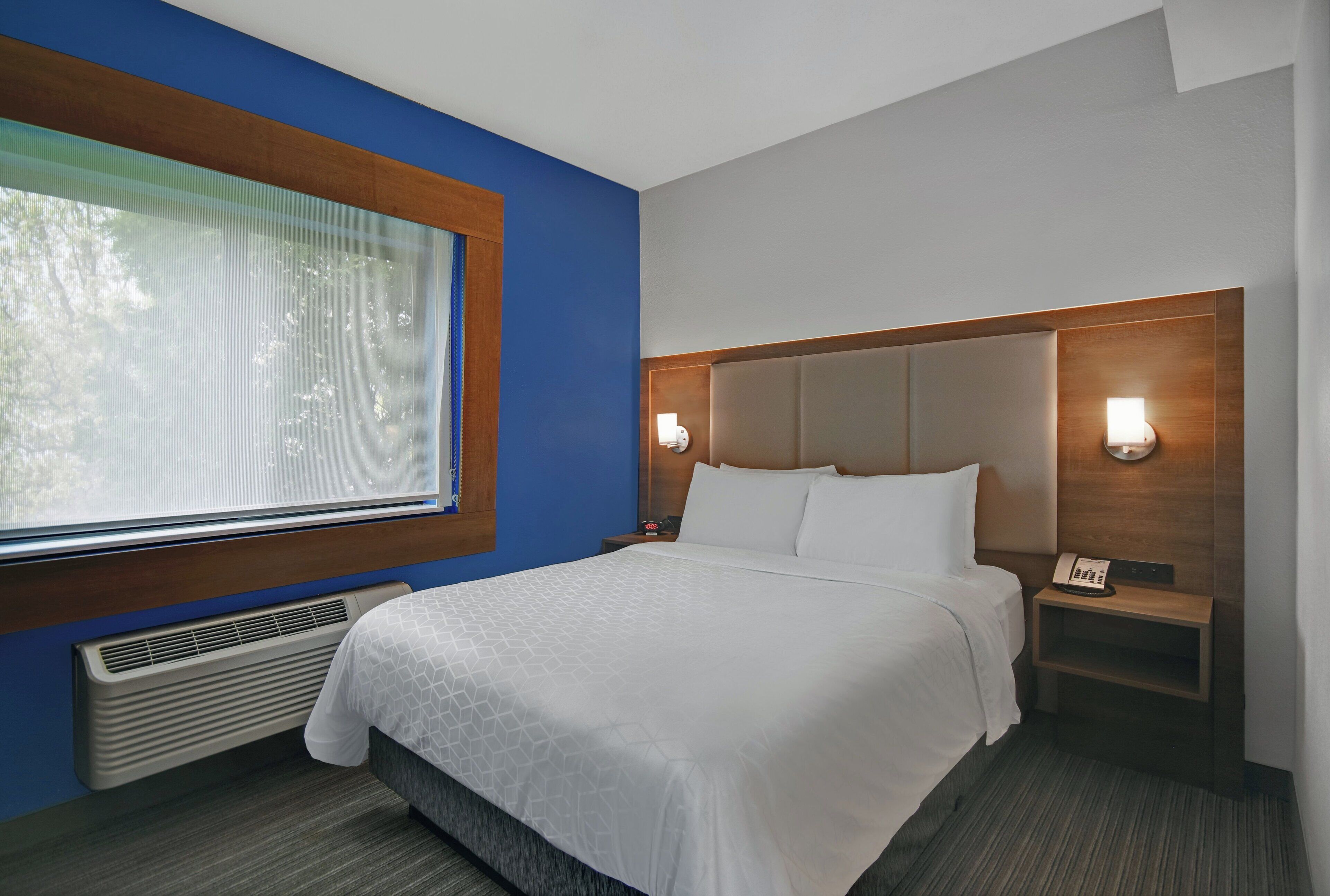 A hotel room with a bed, a nightstand, a telephone, and a window with curtains.