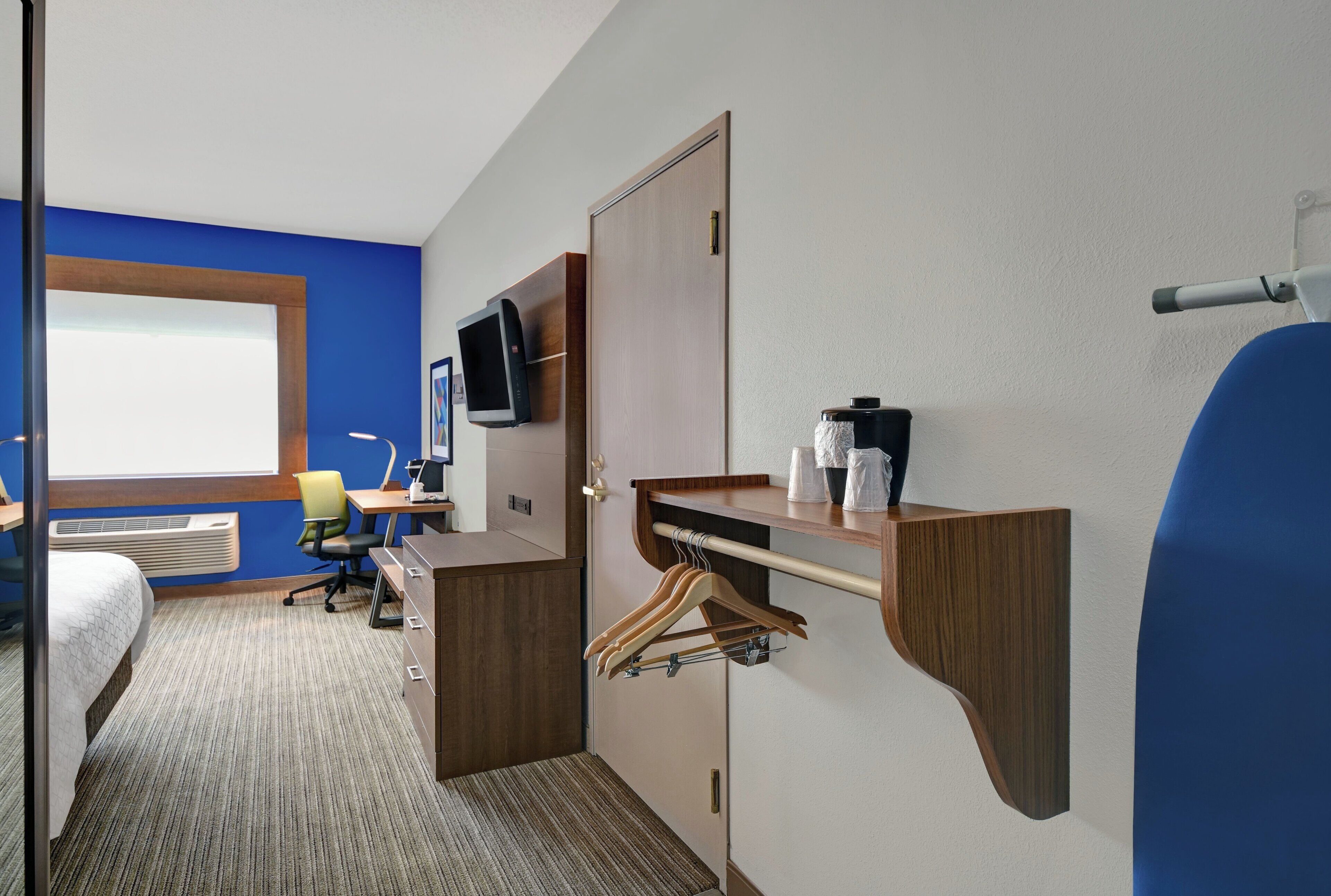 A hotel room with a bed, desk, chair, TV, and a wardrobe.