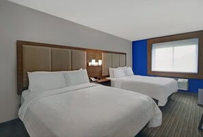 Een hotelkamer met twee bedden, een nachtkastje met telefoon, lamp en een raam met jaloezieën.