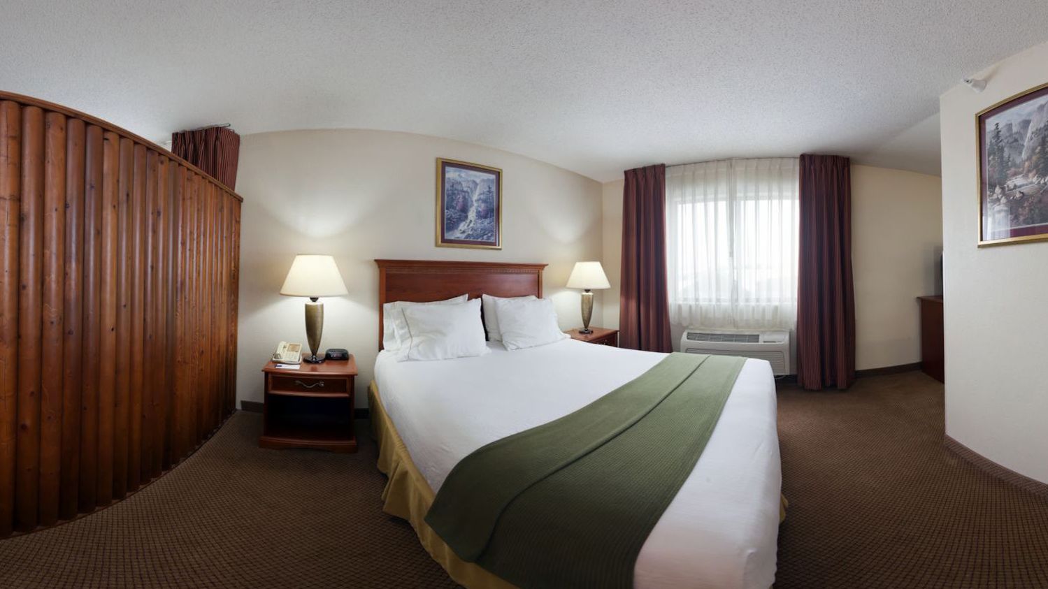 A hotel room with a large bed, two bedside tables with lamps, a window with curtains, and a painting on the wall.