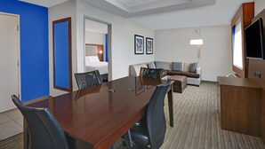 A hotel room with a wooden dining table, black chairs, a sofa, a TV, and a lamp. - Holiday Inn Express Adrian by IHG (Adrian)