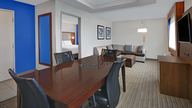 A hotel room with a wooden dining table, black chairs, a sofa, a TV, and a lamp. - Holiday Inn Express Adrian by IHG (Adrian)