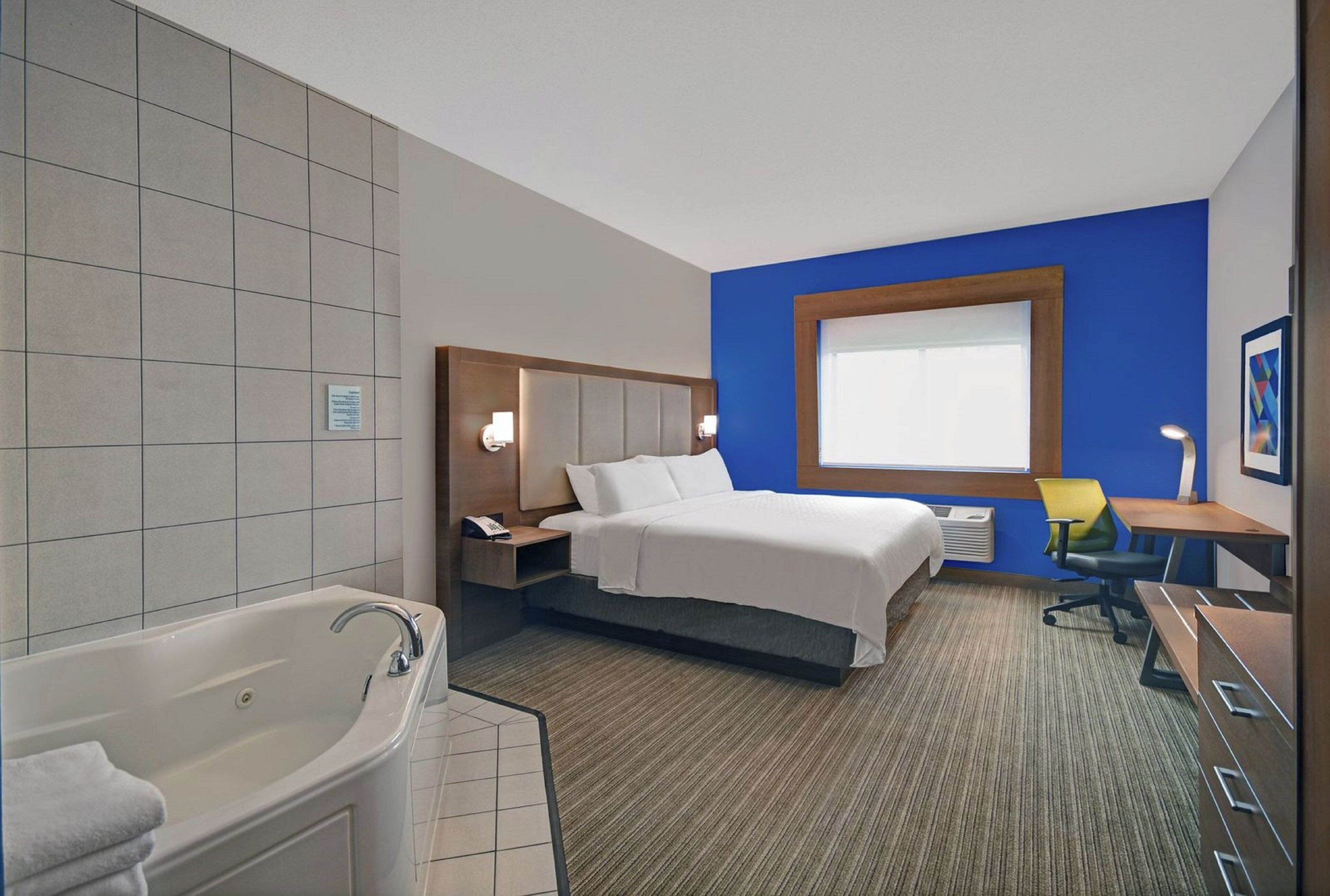 Quarto de hotel com cama grande, banheiro separado com banheira, escrivaninha com cadeira e janela.
