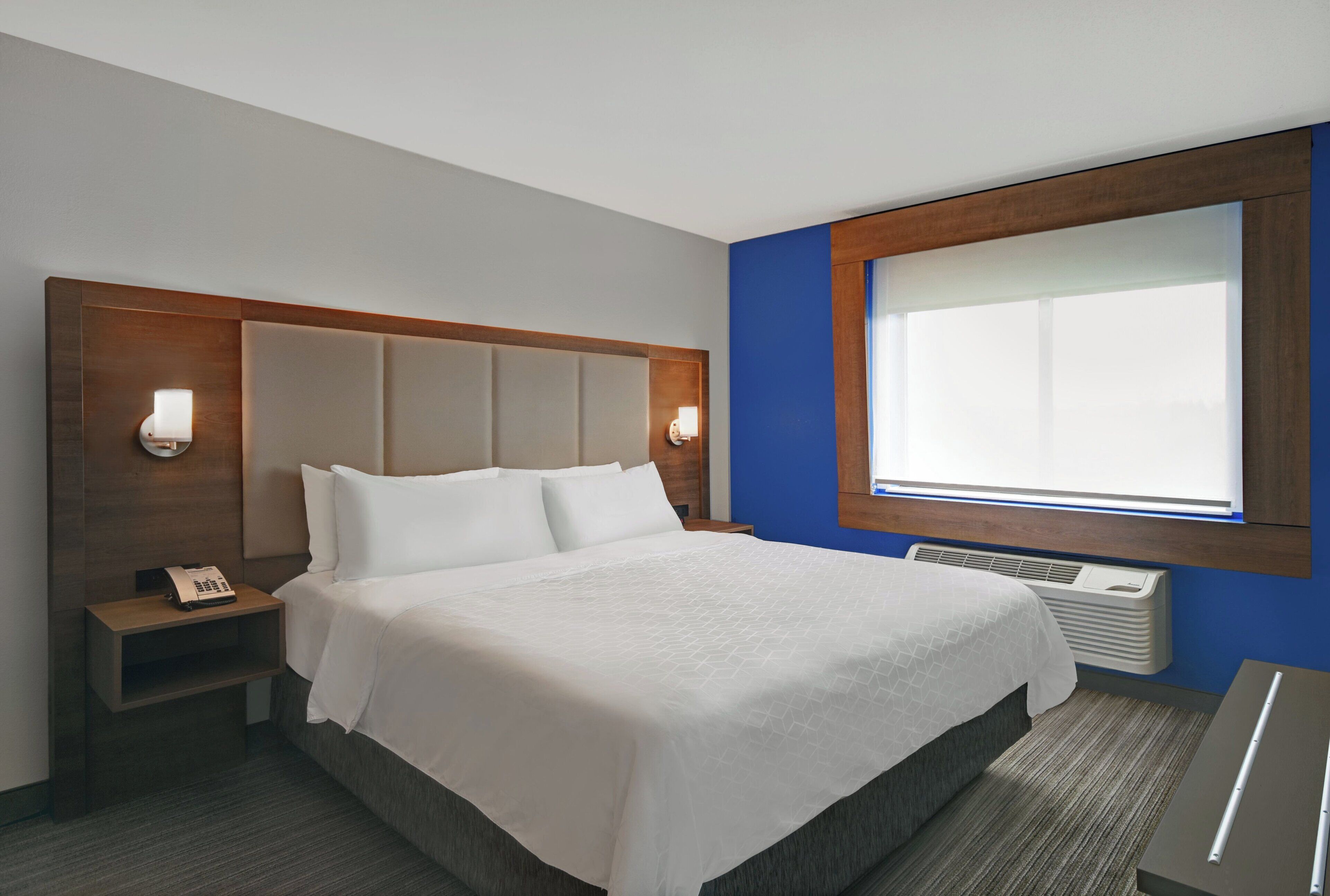 Habitación de hotel con cama, mesita de noche, lámpara y ventana con persianas.