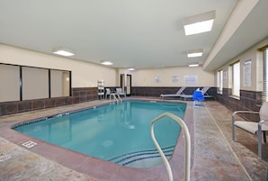 Una piscina interior con suelo de baldosas, una escalera de piscina y sillas de descanso.