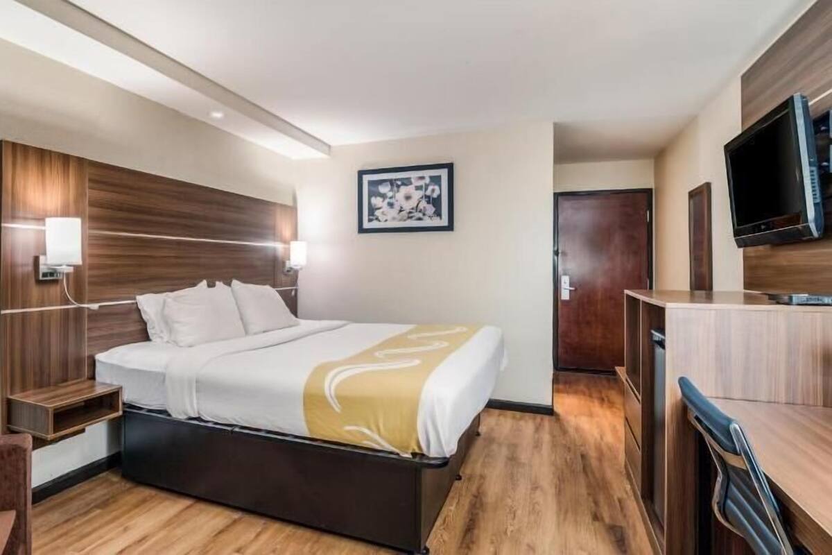 Habitación de hotel con cama, mesitas de noche, un escritorio, una silla, televisión y un cuadro en la pared.