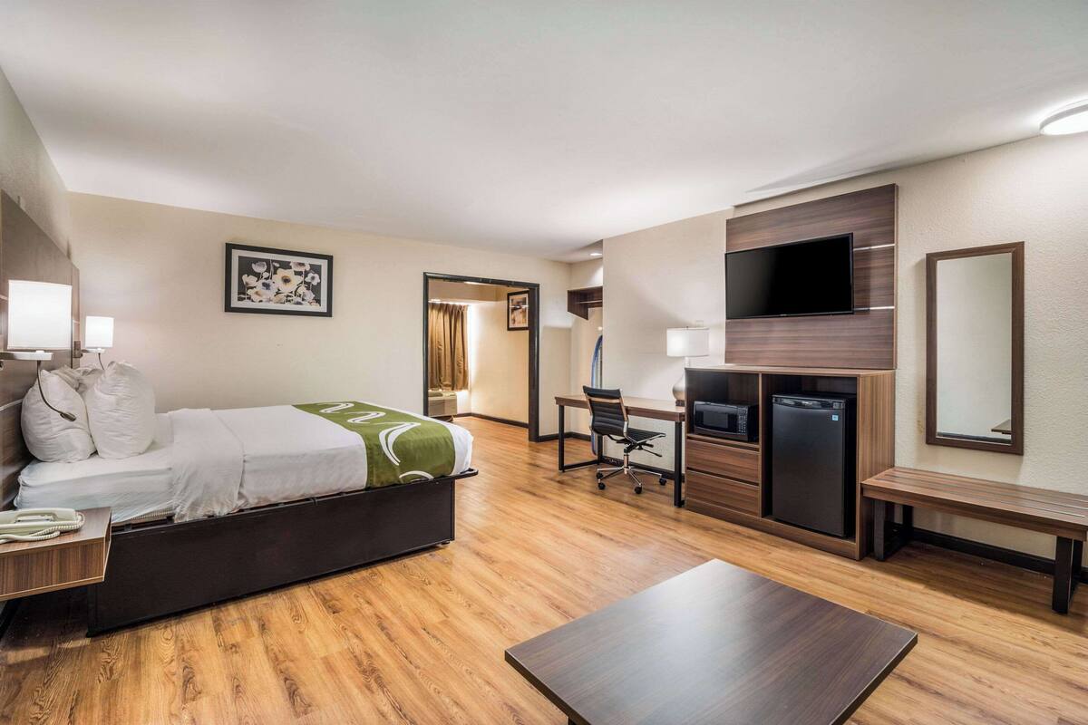 Una habitación de hotel con cama, escritorio, silla, televisor y una pequeña mesa de comedor.