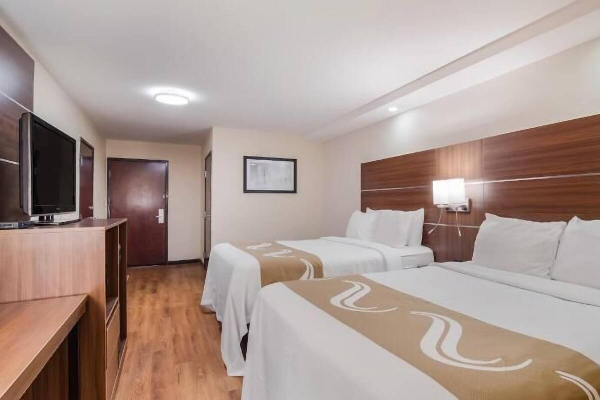 Una habitación de hotel con dos camas, televisión, cabecera de madera y un cuadro enmarcado en la pared.