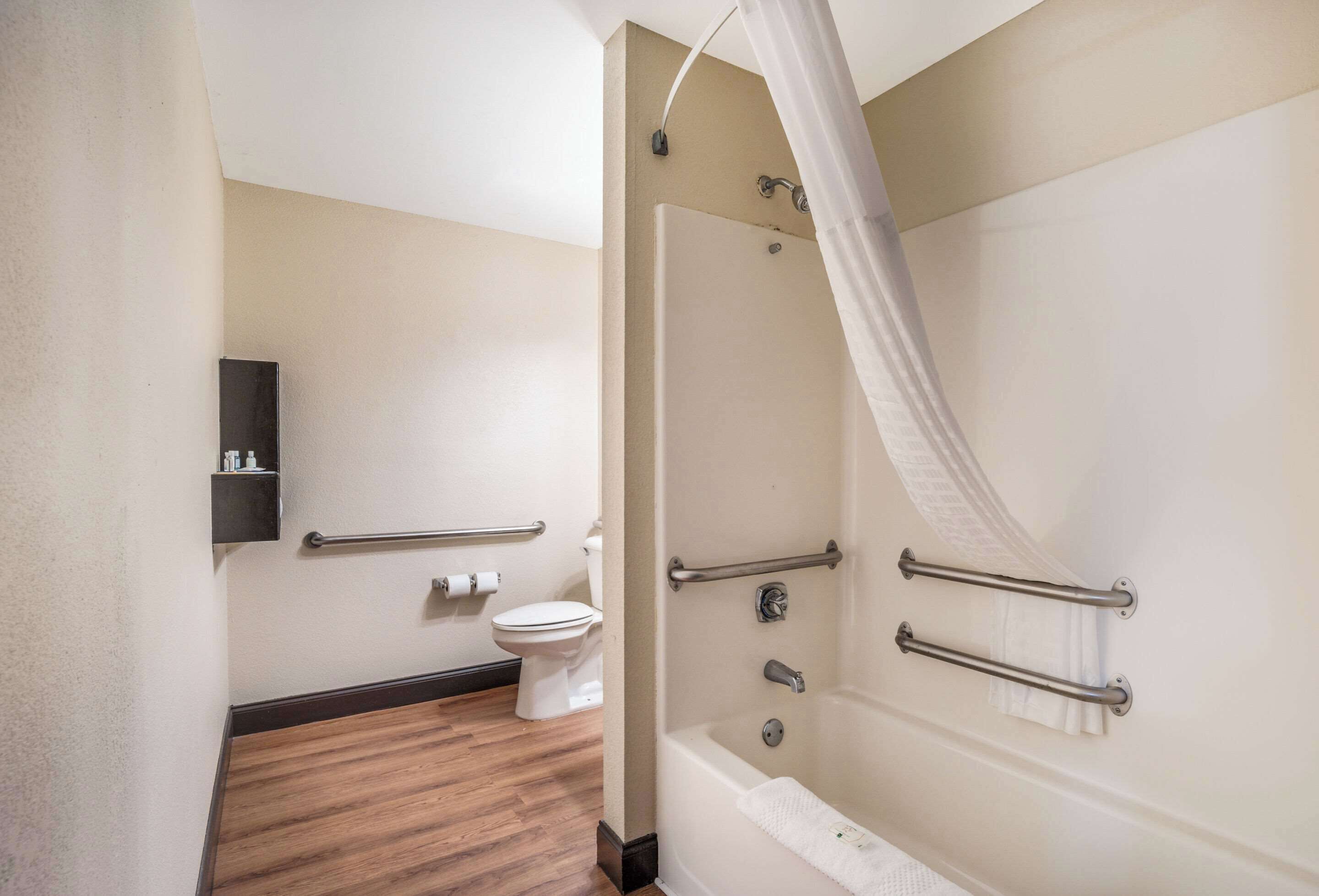 A bathroom with a shower, toilet, and a handrail.