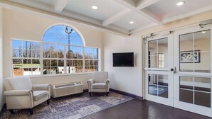 A spacious room with a large arched window, a flat-screen TV mounted on the wall, and a sliding glass door leading to a balcony. - Quality Inn & Suites Augusta Fort Gordon Area (Augusta)