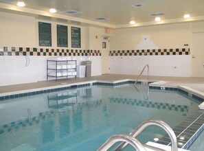 An indoor swimming pool with clear water, tiled walls, and a checkered pattern at the bottom. There are signs indicating lifeguard duty and occupant capacity. - Hilton Garden Inn Addison (Addison)