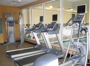 A fitness center with treadmills, a weight machine, and a mirrored wall. - Hilton Garden Inn Addison (Addison)