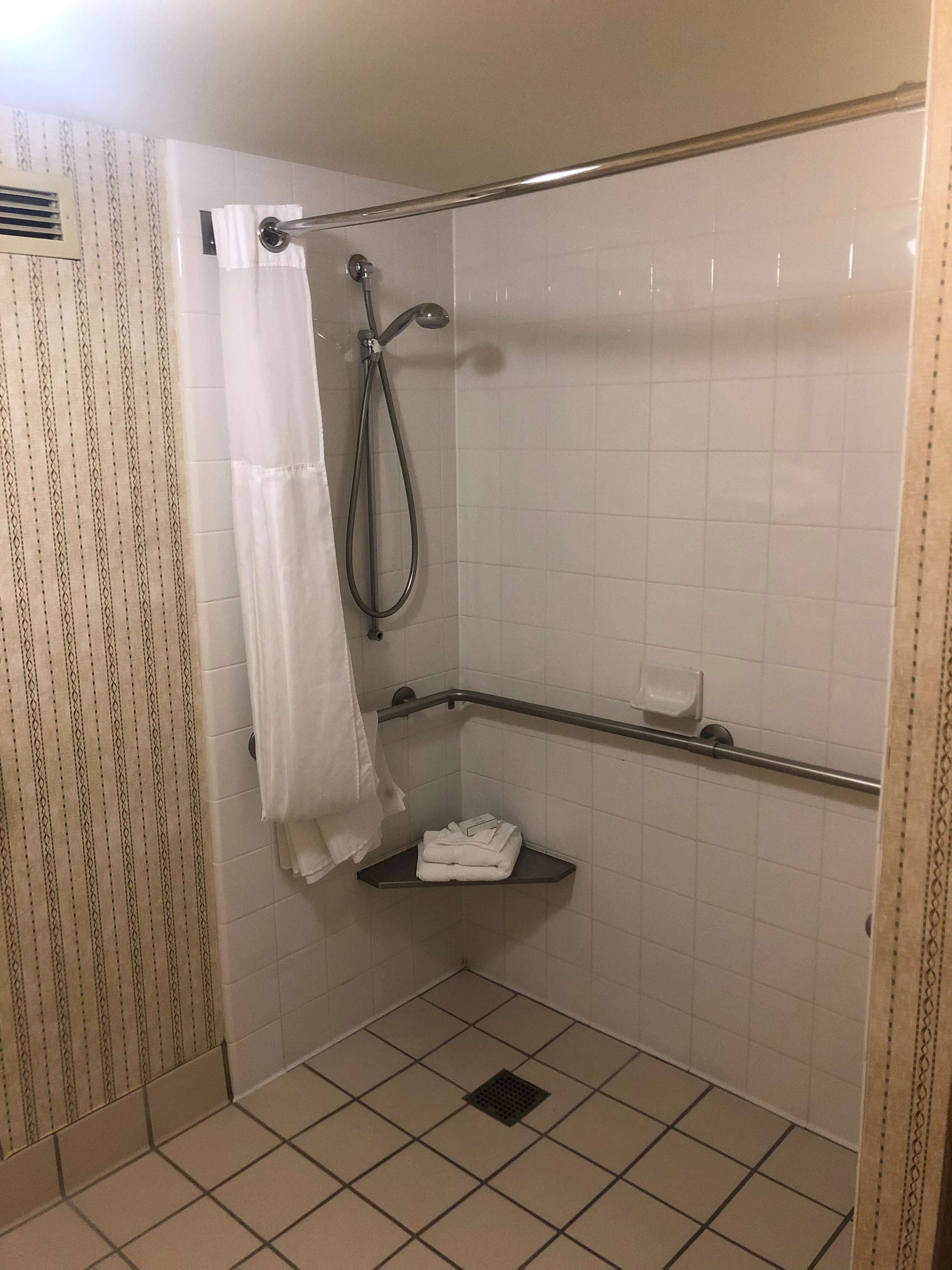A small, tiled shower area with a showerhead, a towel rack, and a shelf.