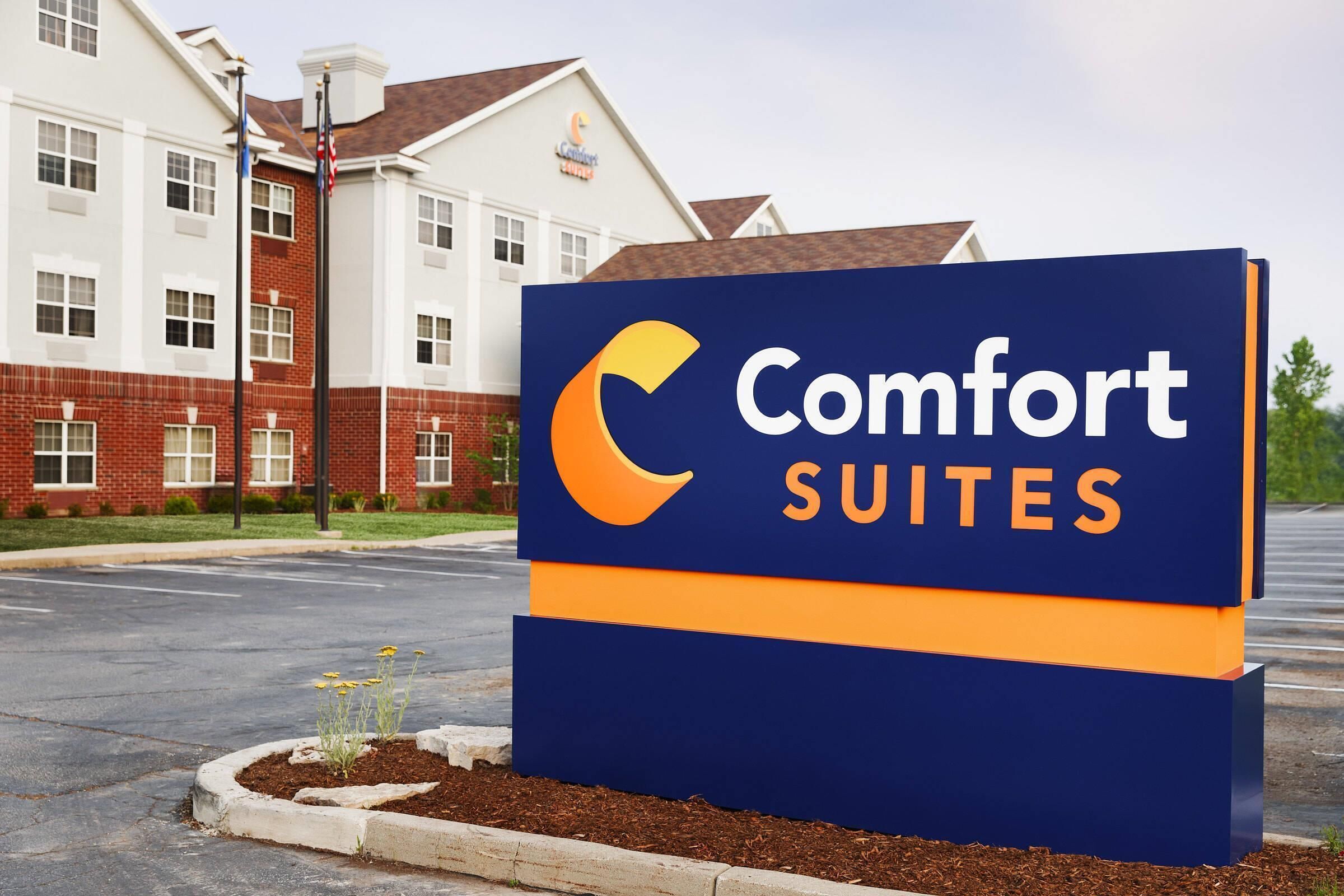 Naamplaatje voor Comfort Suites, met een modern gebouw op de achtergrond.