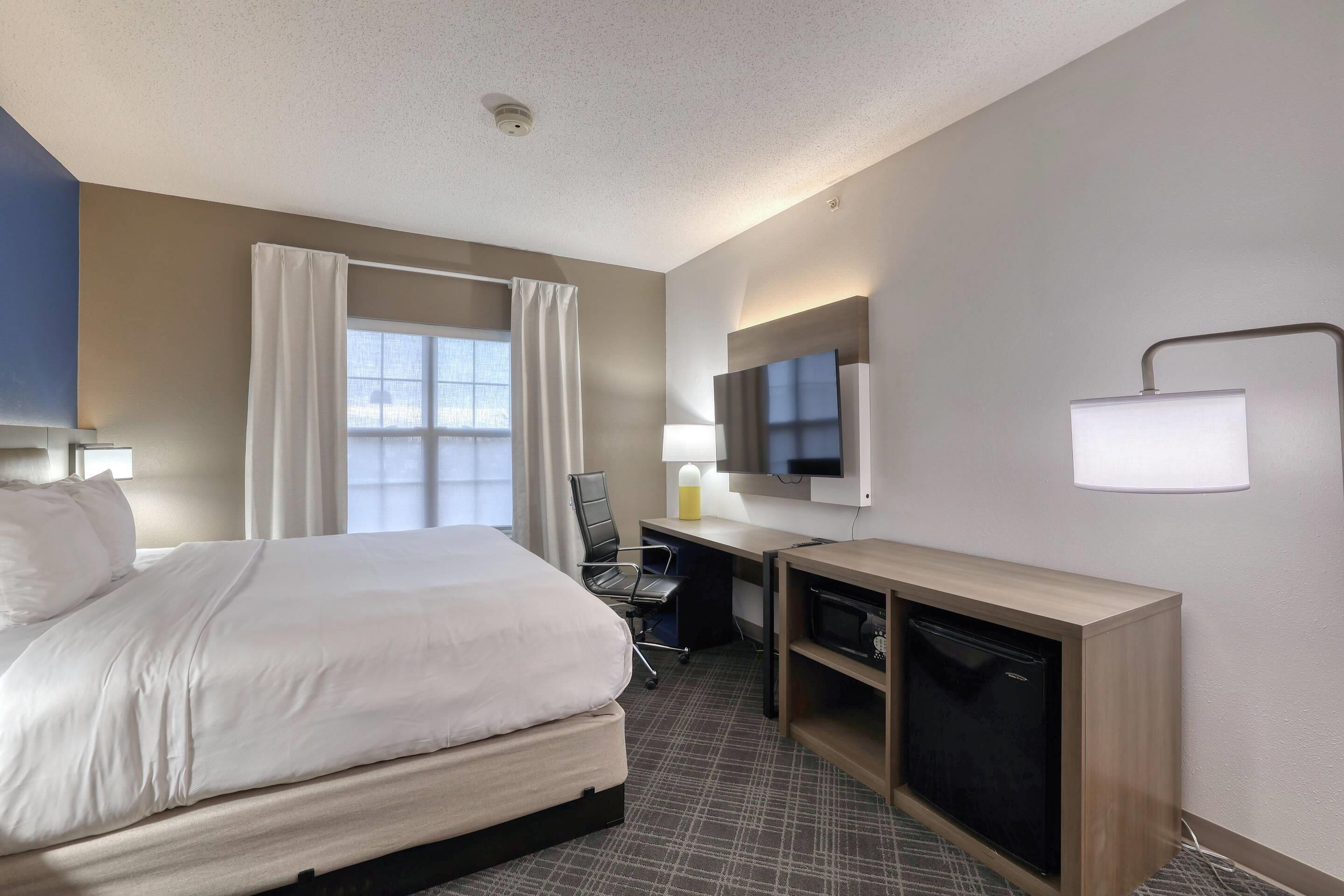 Ein Hotelzimmer mit Bett, Schreibtisch, Stuhl, Fernseher und einer Minibar.