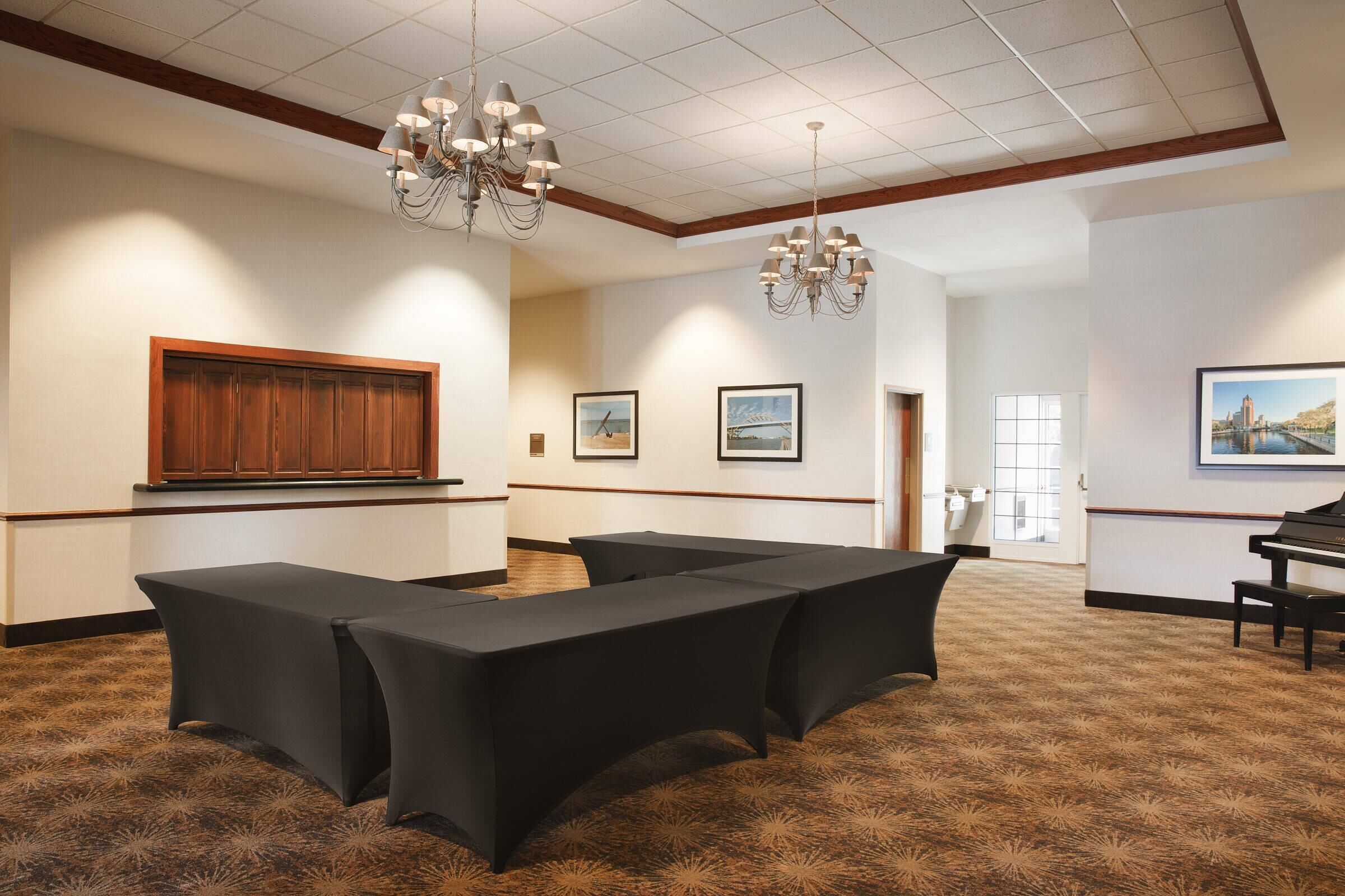 Un salón de conferencias con mesas, un piano, cuadros enmarcados y un panel de madera en la pared.