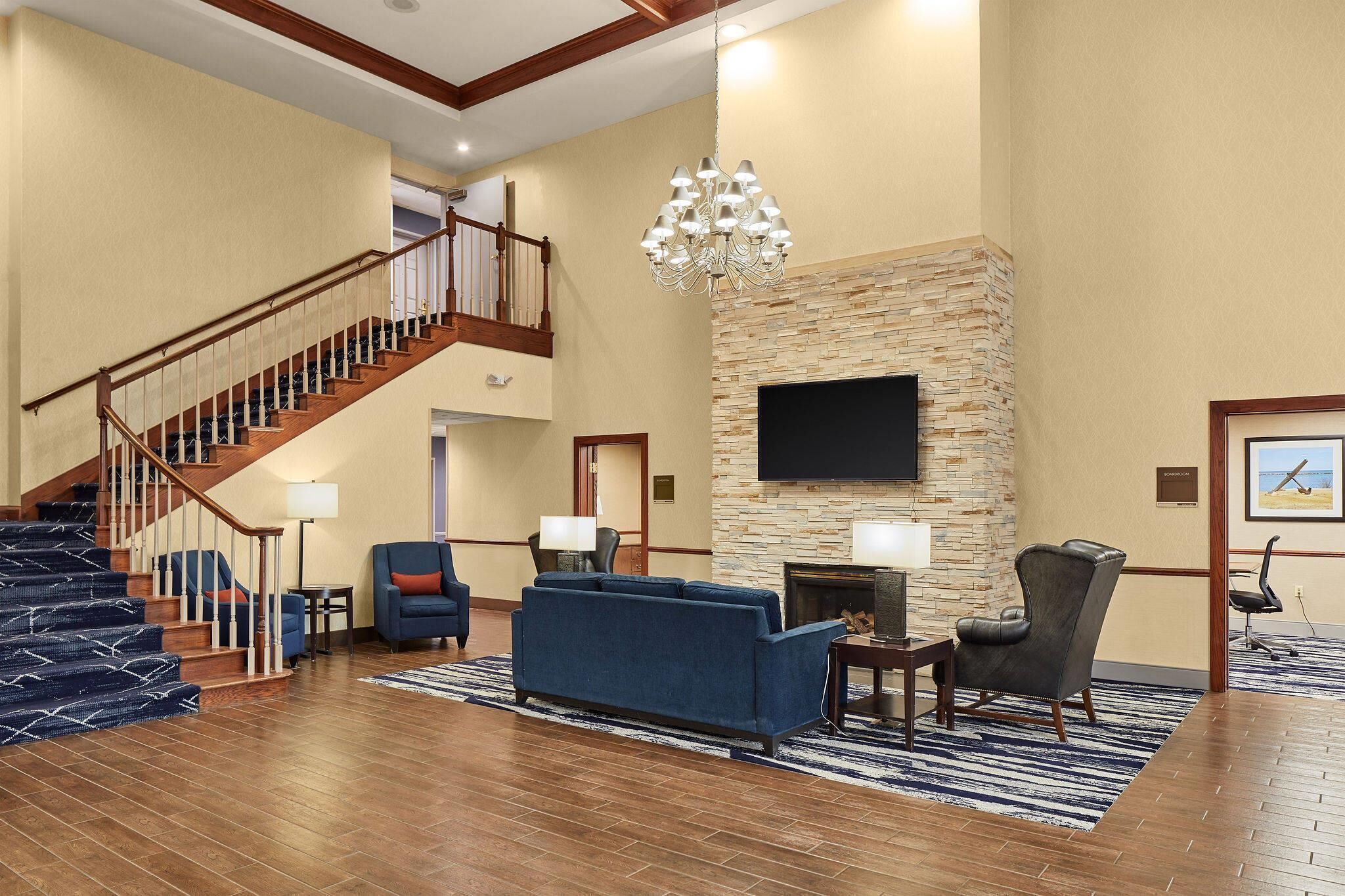 A spacious lobby with a staircase, a stone fireplace, a flat-screen TV, and a blue sofa.