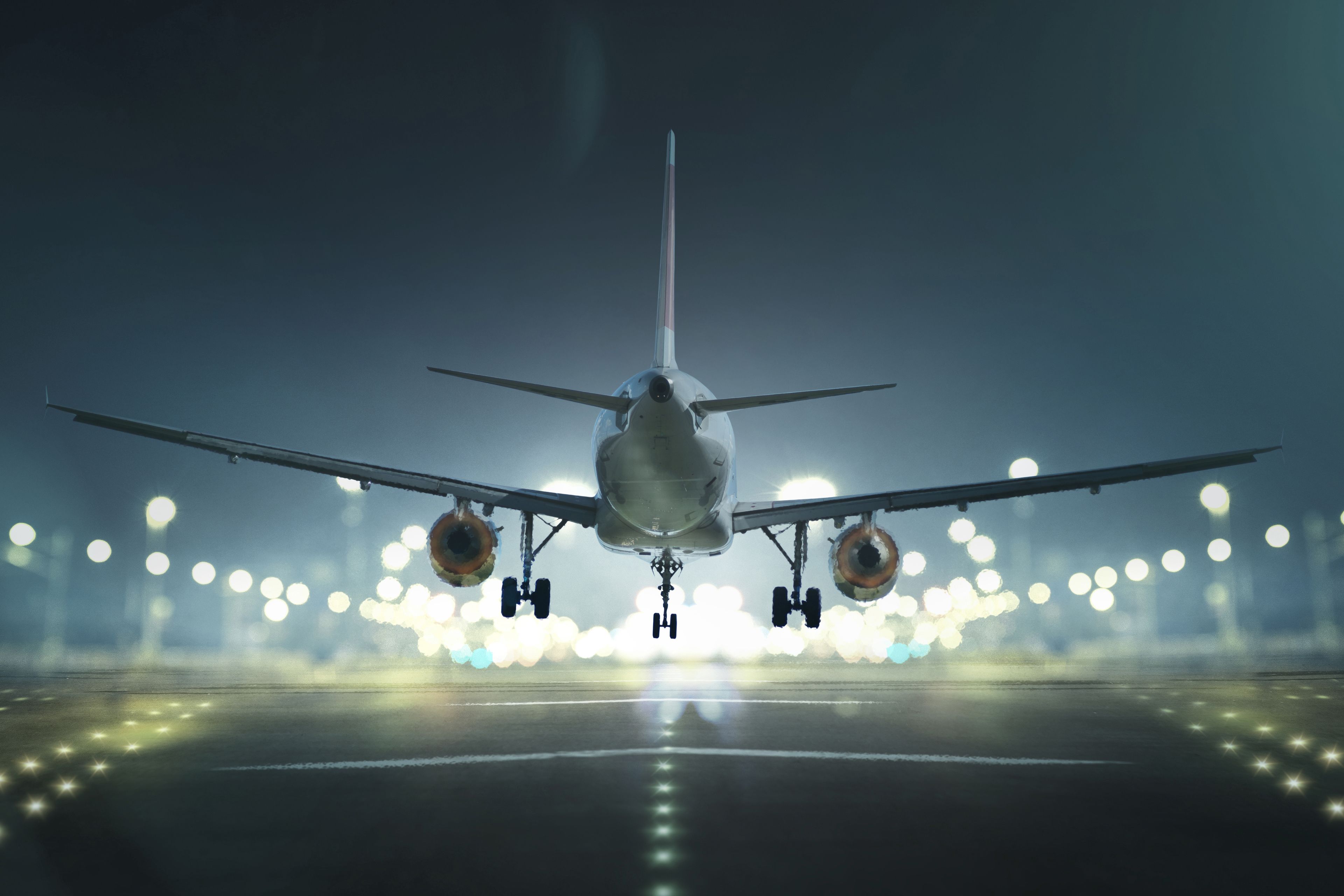 An airplane on the runway with its landing gear extended, lights on, and a blurred background of airport lights.