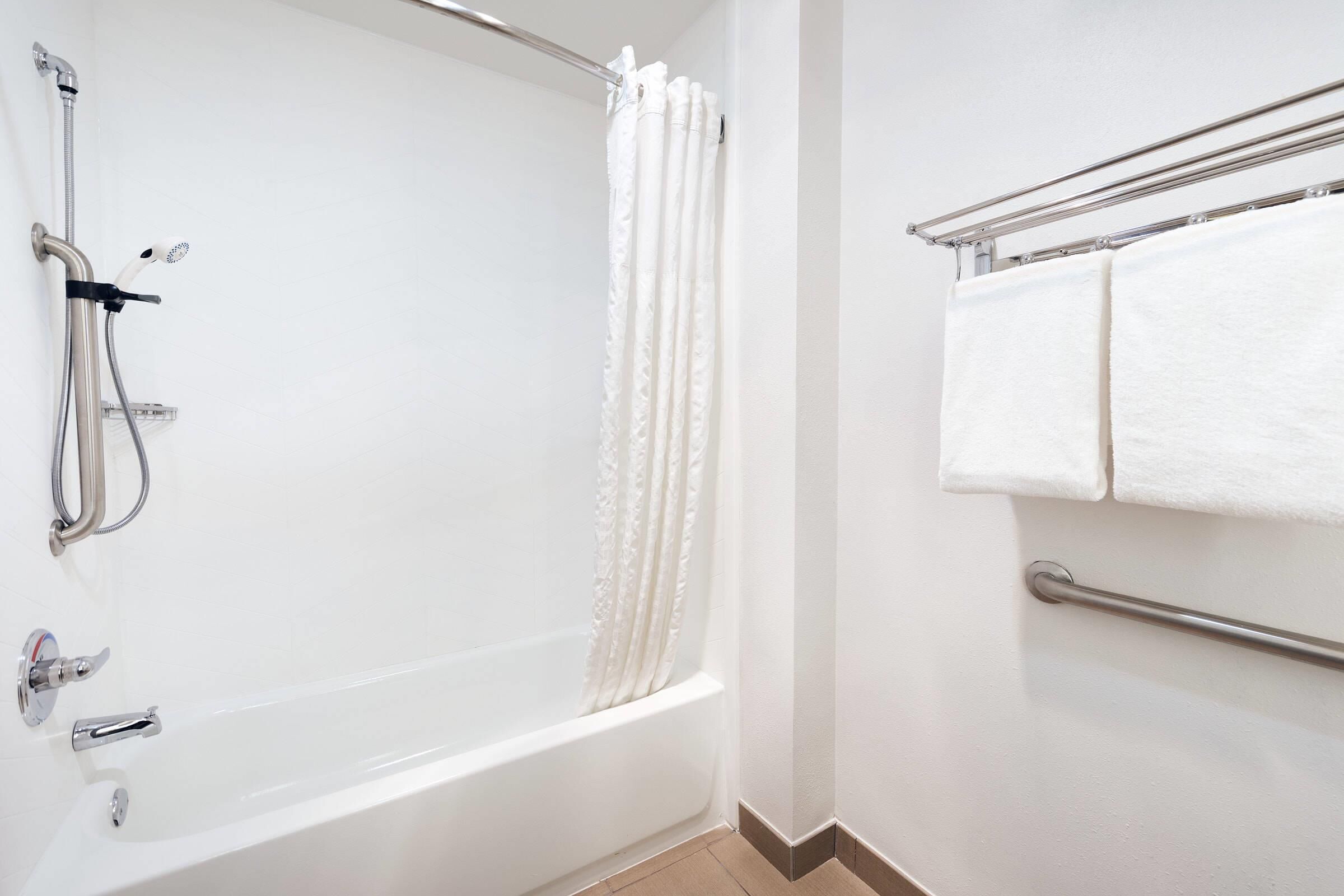 A white bathtub with a showerhead, a towel rack with two towels, and a grab bar.