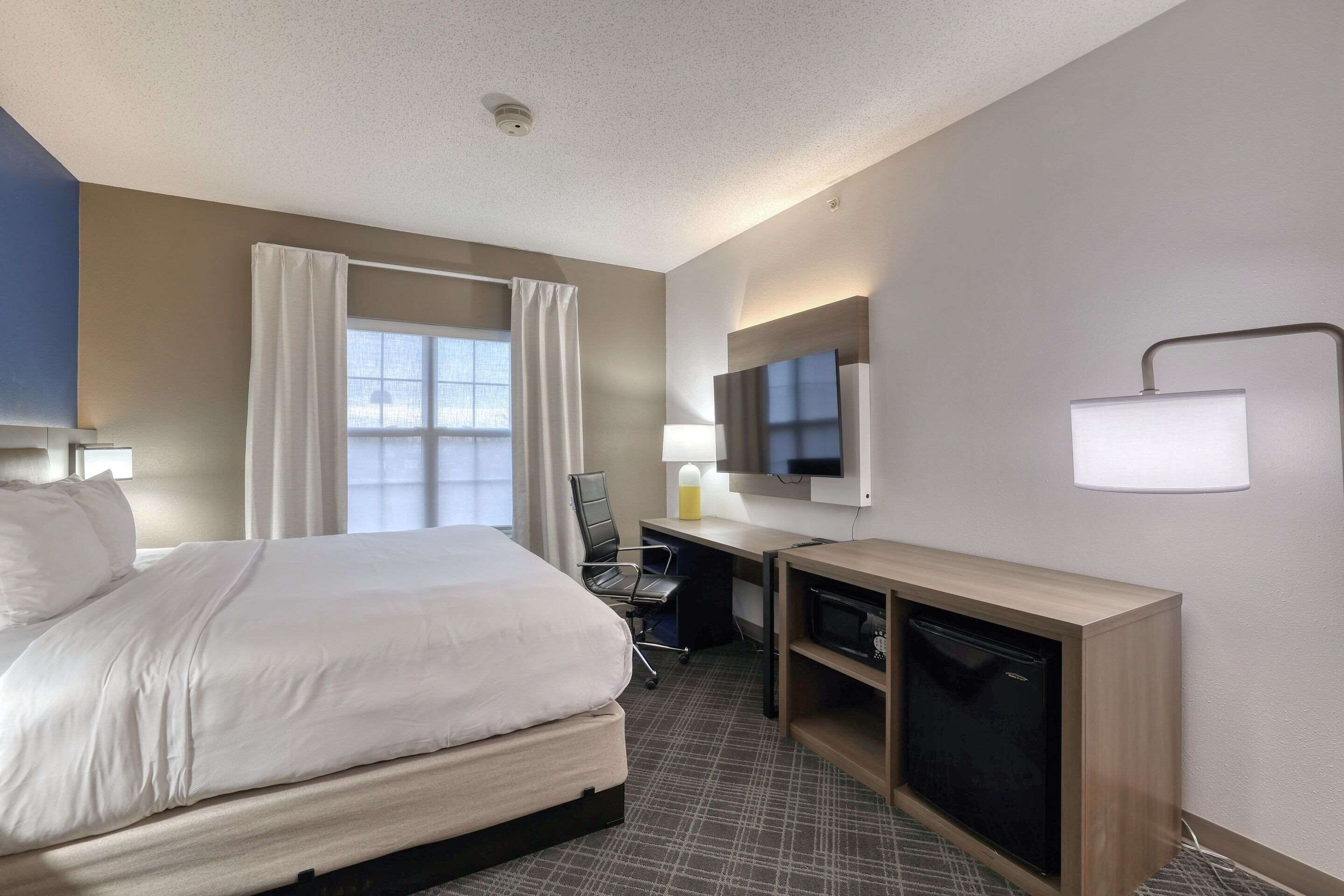 Une chambre d’hôtel équipée d’un lit, d’un bureau, d’une chaise, d’une télévision et d’une petite kitchenette.
