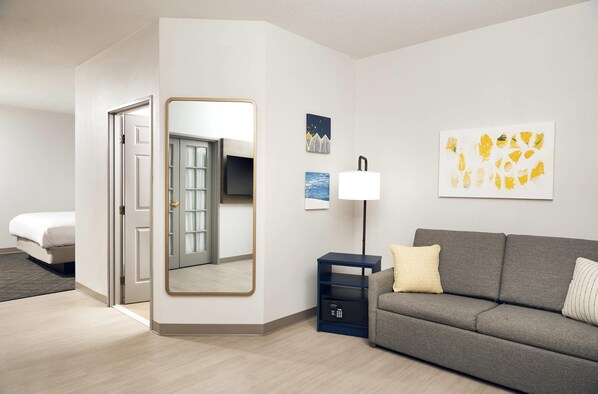 A modern hotel room with a bed, a sofa, a desk with a lamp, and artwork on the walls. - Comfort Suites Milwaukee Airport (Oak Creek)