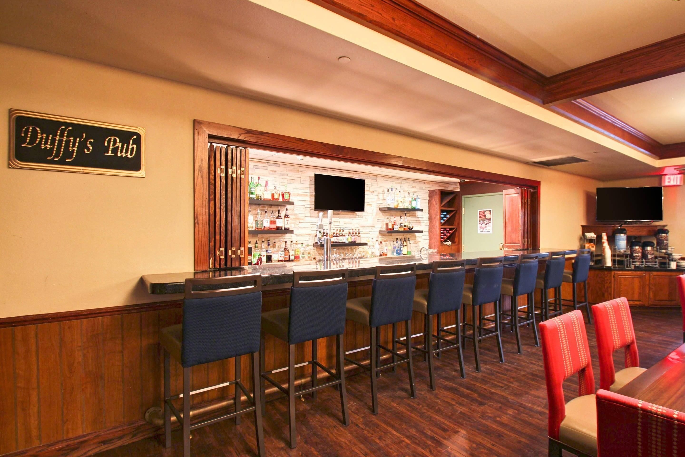 Un espace bar avec une enseigne indiquant « Duffy’s Pub », des tabourets de bar, un téléviseur et un comptoir où sont exposées diverses bouteilles.