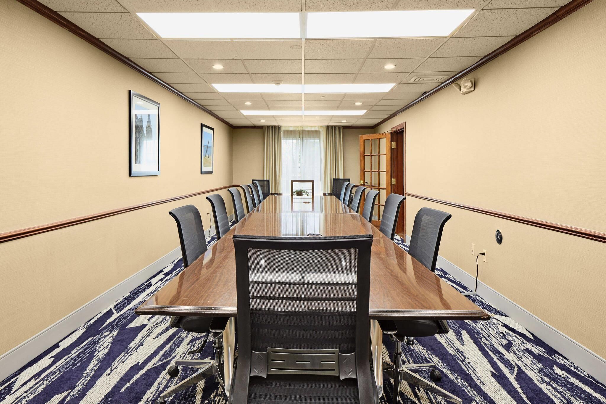 A conference room with a long table, chairs, and a carpeted floor.
