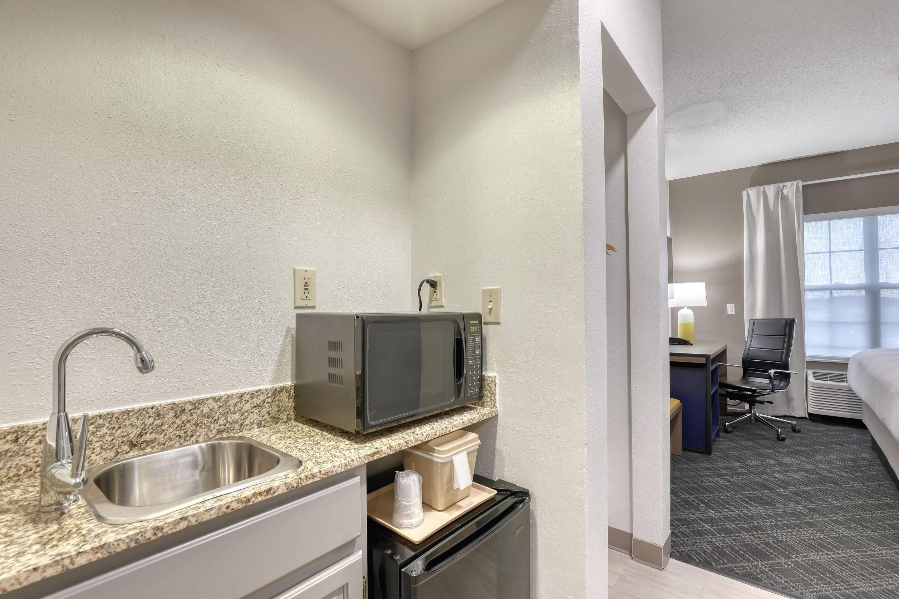 Habitación de hotel compacta con kitchenette, que incluye un lavamanos, microondas y un refrigerador pequeño.