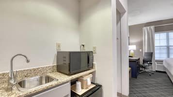 Habitación de hotel compacta con kitchenette, que incluye un lavamanos, microondas y un refrigerador pequeño.