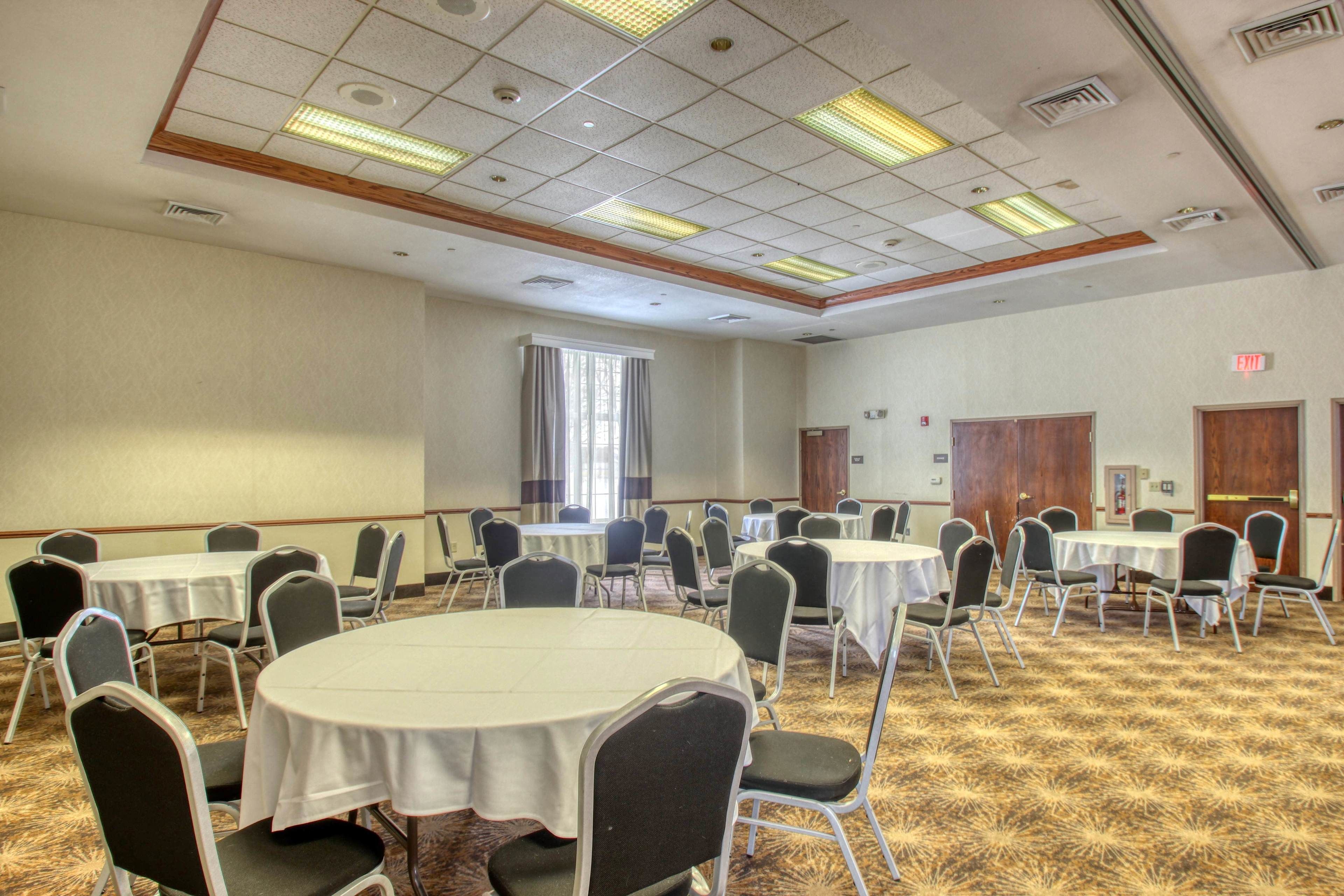 A conference room with multiple round tables and chairs, a carpeted floor, and a ceiling with fluorescent lights.