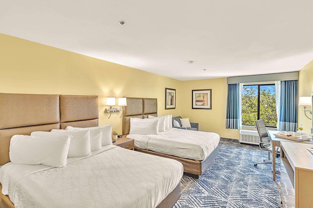 A hotel room with two beds, a desk, and a window with curtains.
