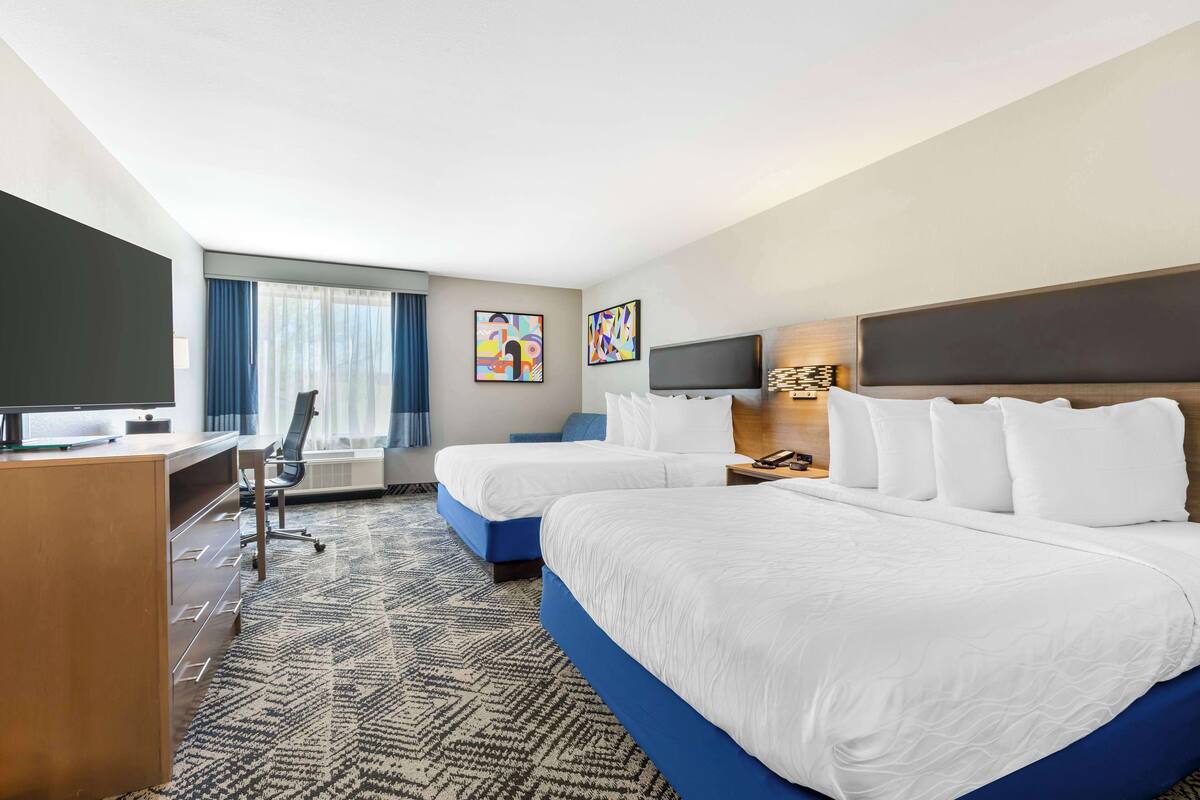 A hotel room with two beds, a desk, a TV, and artwork on the walls.