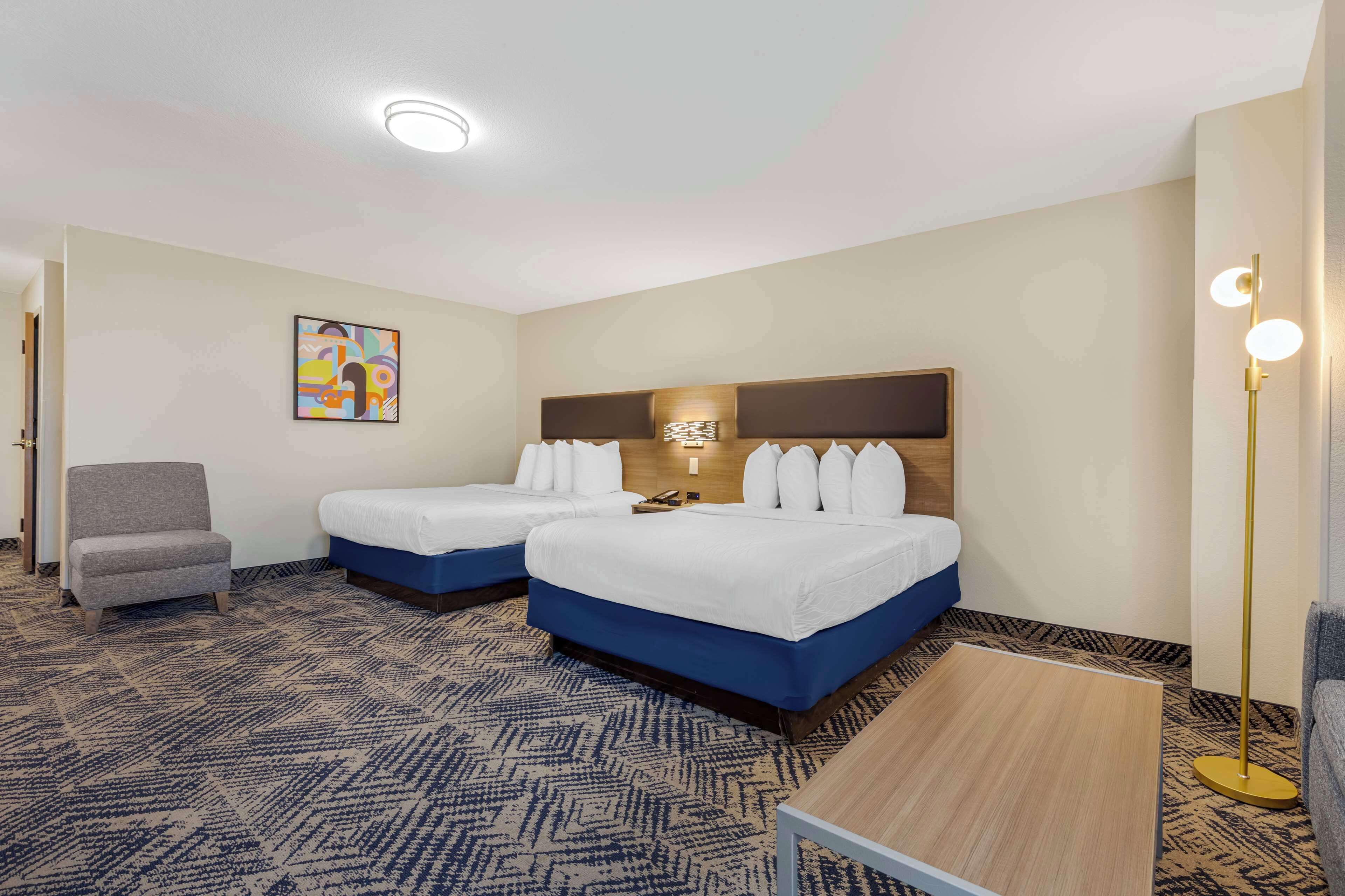 Una habitación de hotel con dos camas, una silla, un escritorio y una lámpara de pie.