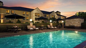 A swimming pool with lounge chairs and umbrellas, surrounded by a hotel building with stone accents and multiple windows. - Best Western Plus Lewisville Flower Mound (Lewisville)