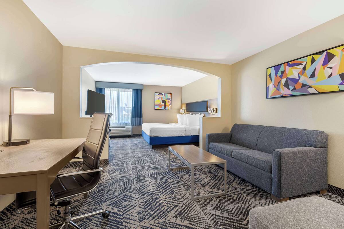 A hotel room with a desk, a sofa, a bed, and a TV.