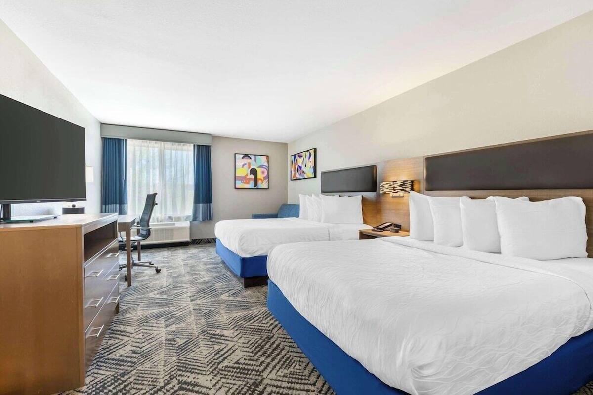 A hotel room with two beds, a desk, a chair, a TV, and artwork on the walls.
