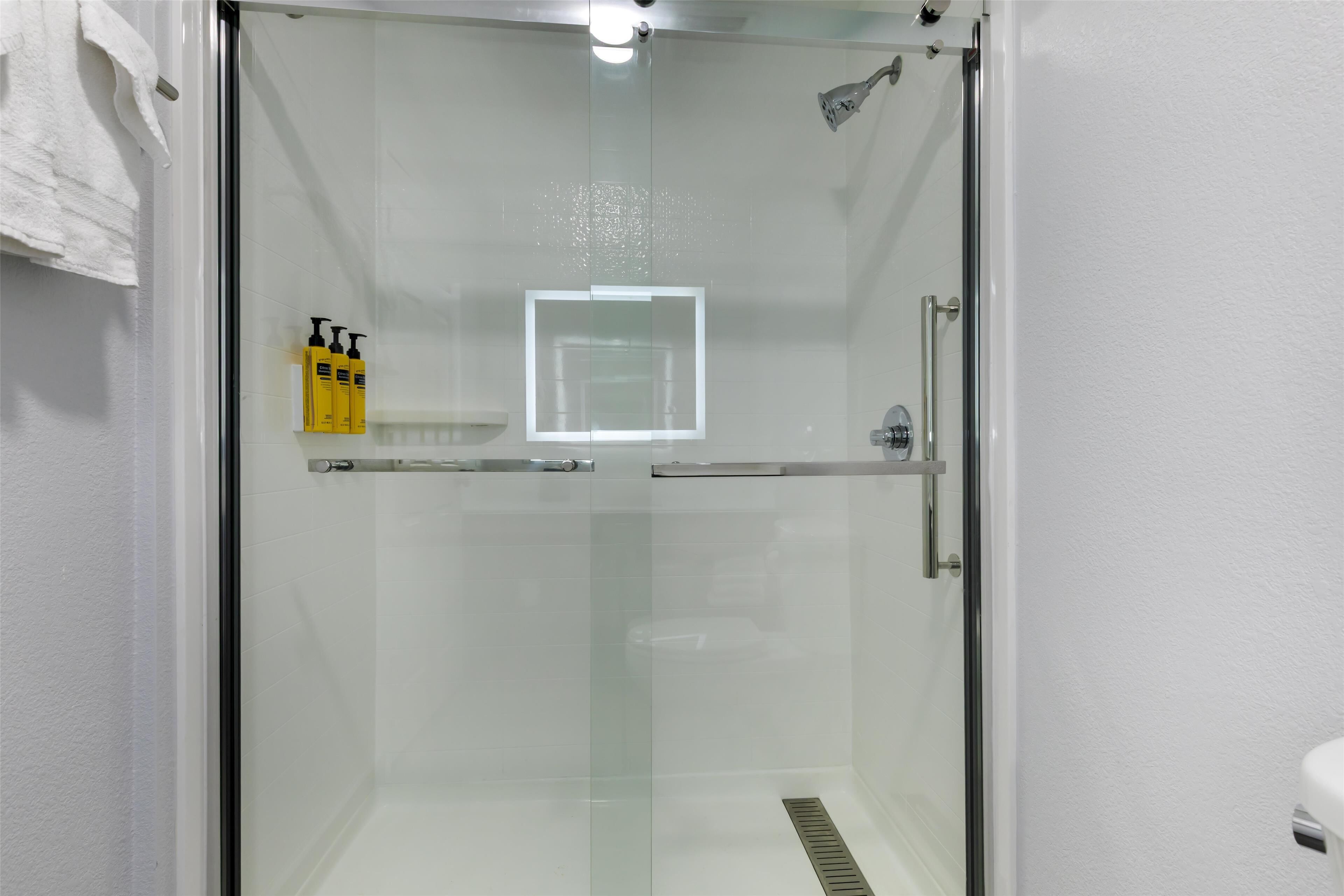 A glass-enclosed shower area with a white tiled wall, a glass door, and a white towel hanging on the left.