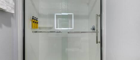A glass-enclosed shower area with a white tiled wall, a glass door, and a white towel hanging on the left.
