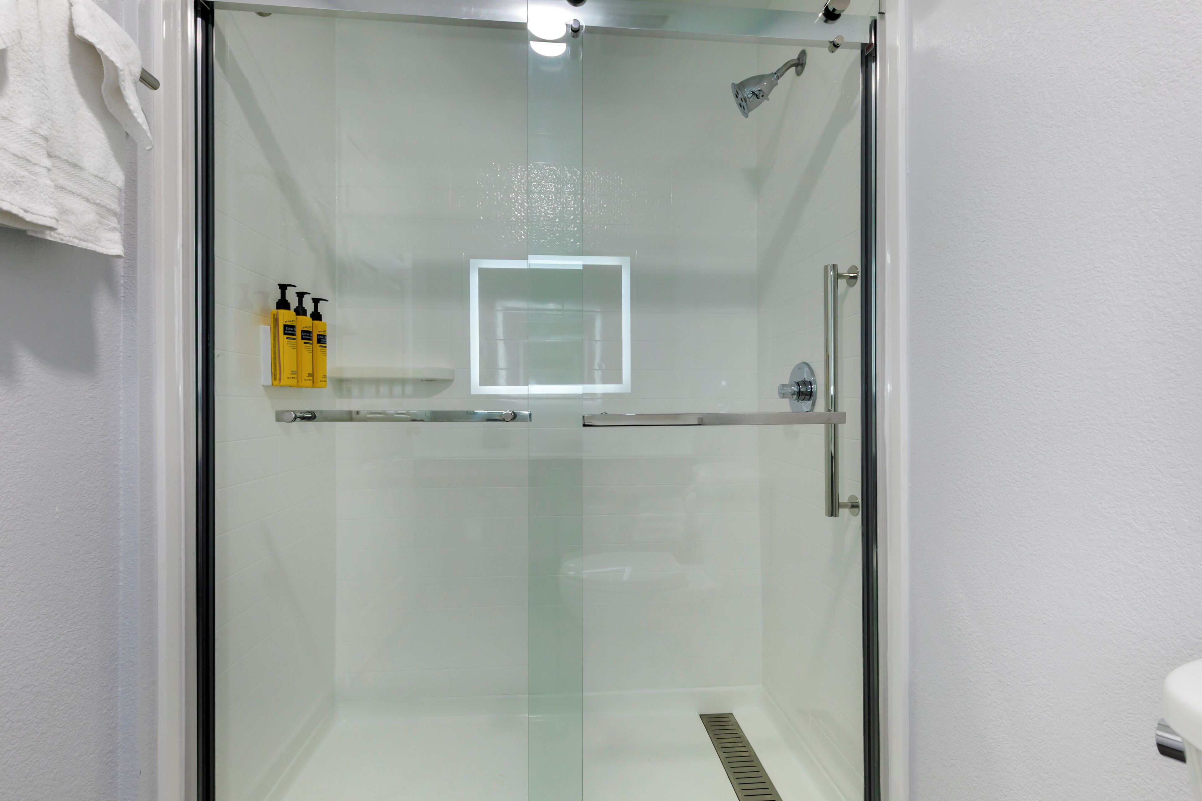 Une douche fermée par des parois de verre, avec un mur recouvert de carreaux blancs, une porte en verre et un pommeau de douche.