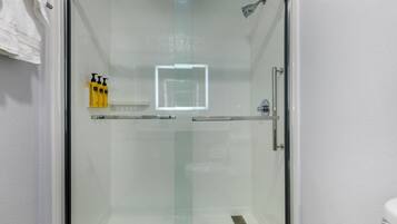 Una ducha con mampara de vidrio, pared de azulejos blancos y ducha.
