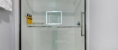 Une douche fermée par des parois de verre, avec un mur recouvert de carreaux blancs, une porte en verre et un pommeau de douche.